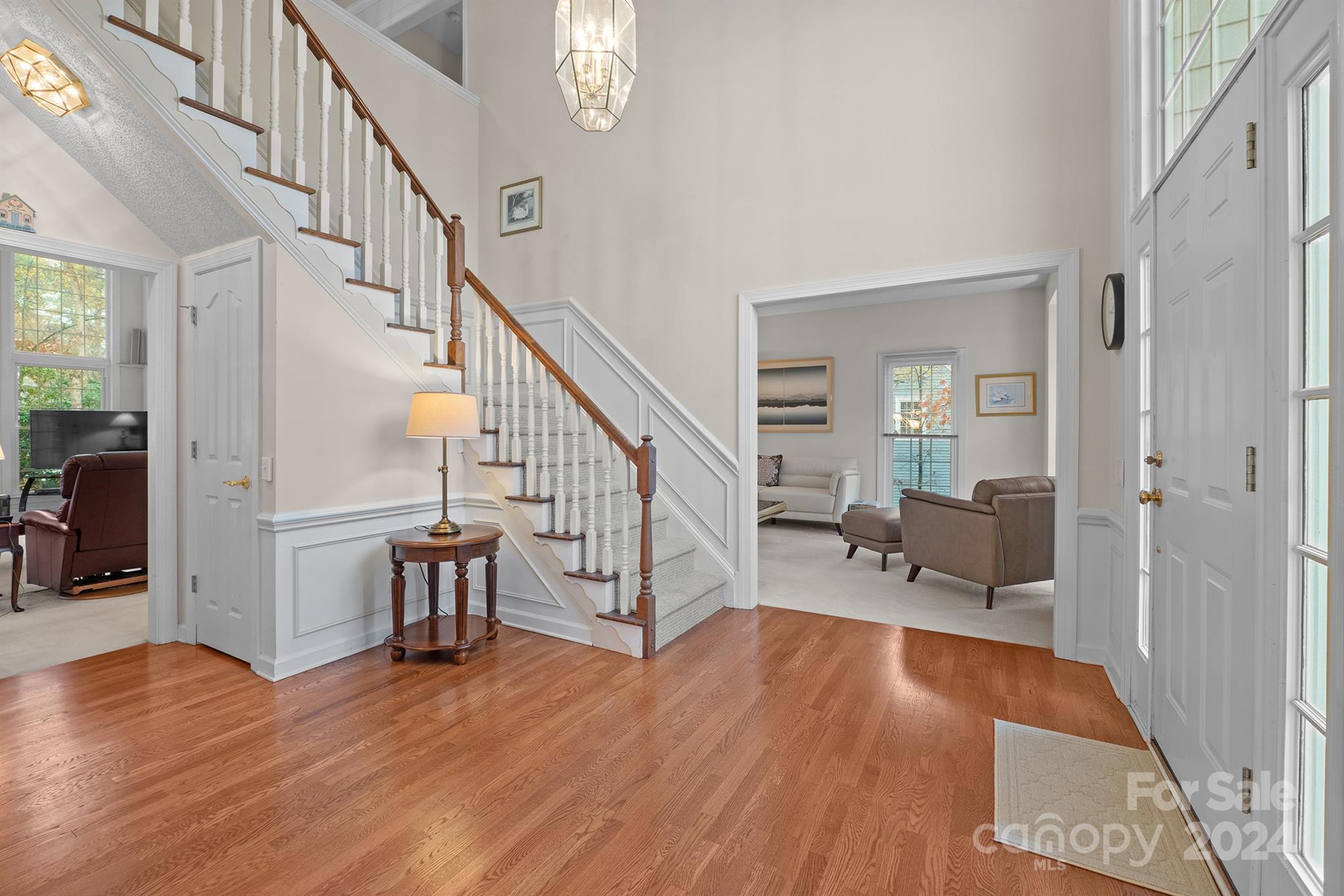 Elegant entryway of a Harrisburg, NC home at 7681 Orchard Park Cir, featuring hardwood floors, a grand staircase, and an open foyer leading to a cozy sitting area...