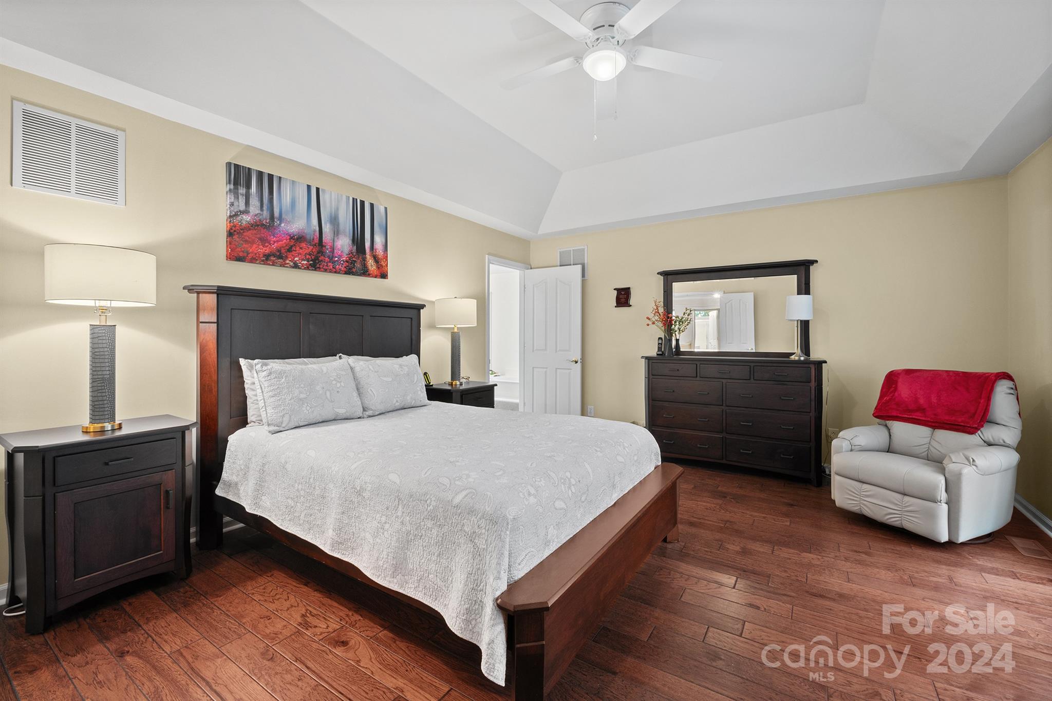 Spacious master bedroom in a Harrisburg, NC home at 7681 Orchard Park Cir, featuring a tray ceiling, hardwood floors, and a warm, inviting atmosphere with modern furnishings...