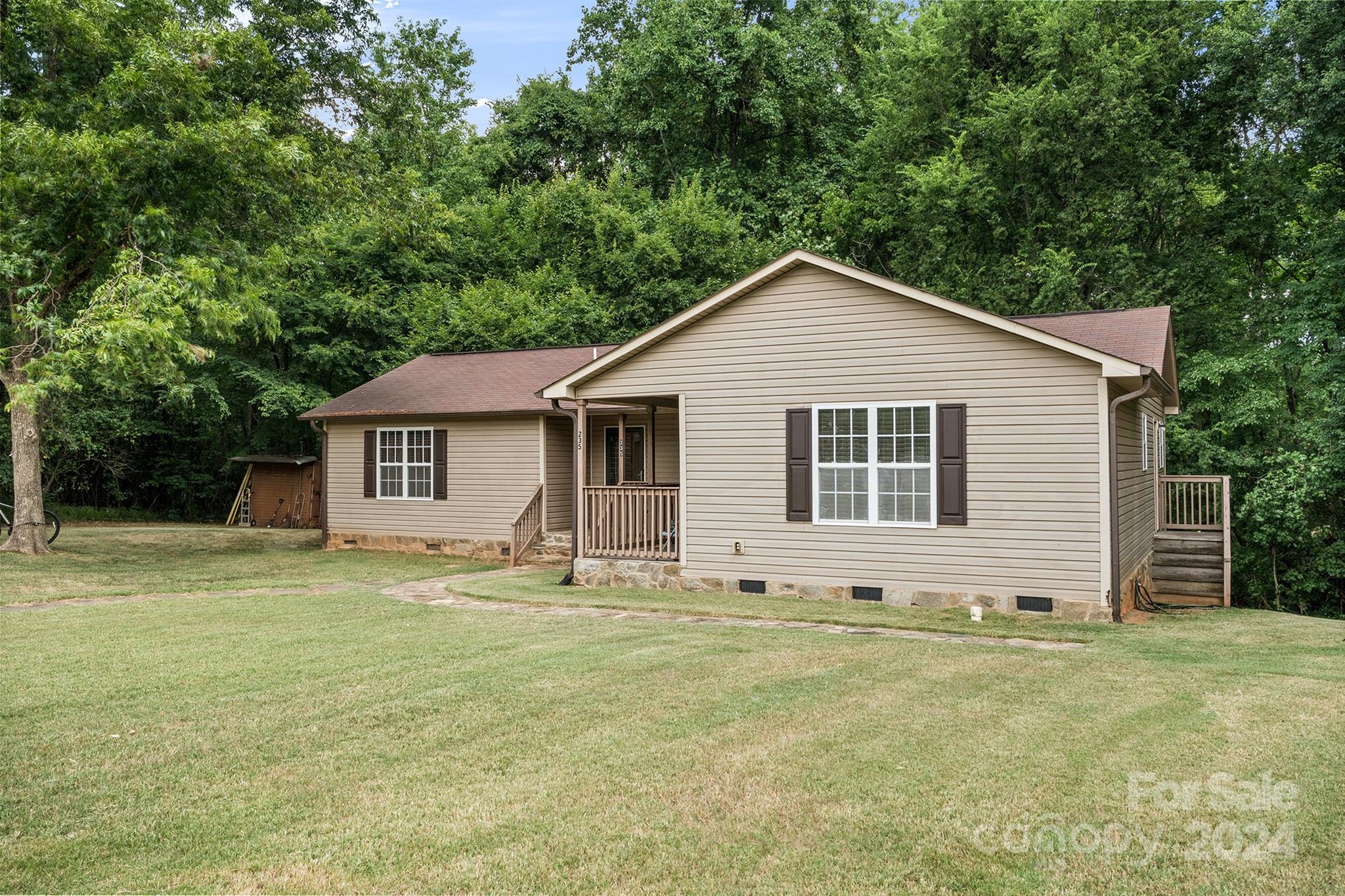 The charming front exterior of a Charlotte, NC home for sale at 231 Nance Rd, featuring a single-story ranch-style design, a welcoming covered porch, large front windows, and a spacious lawn with mature trees...