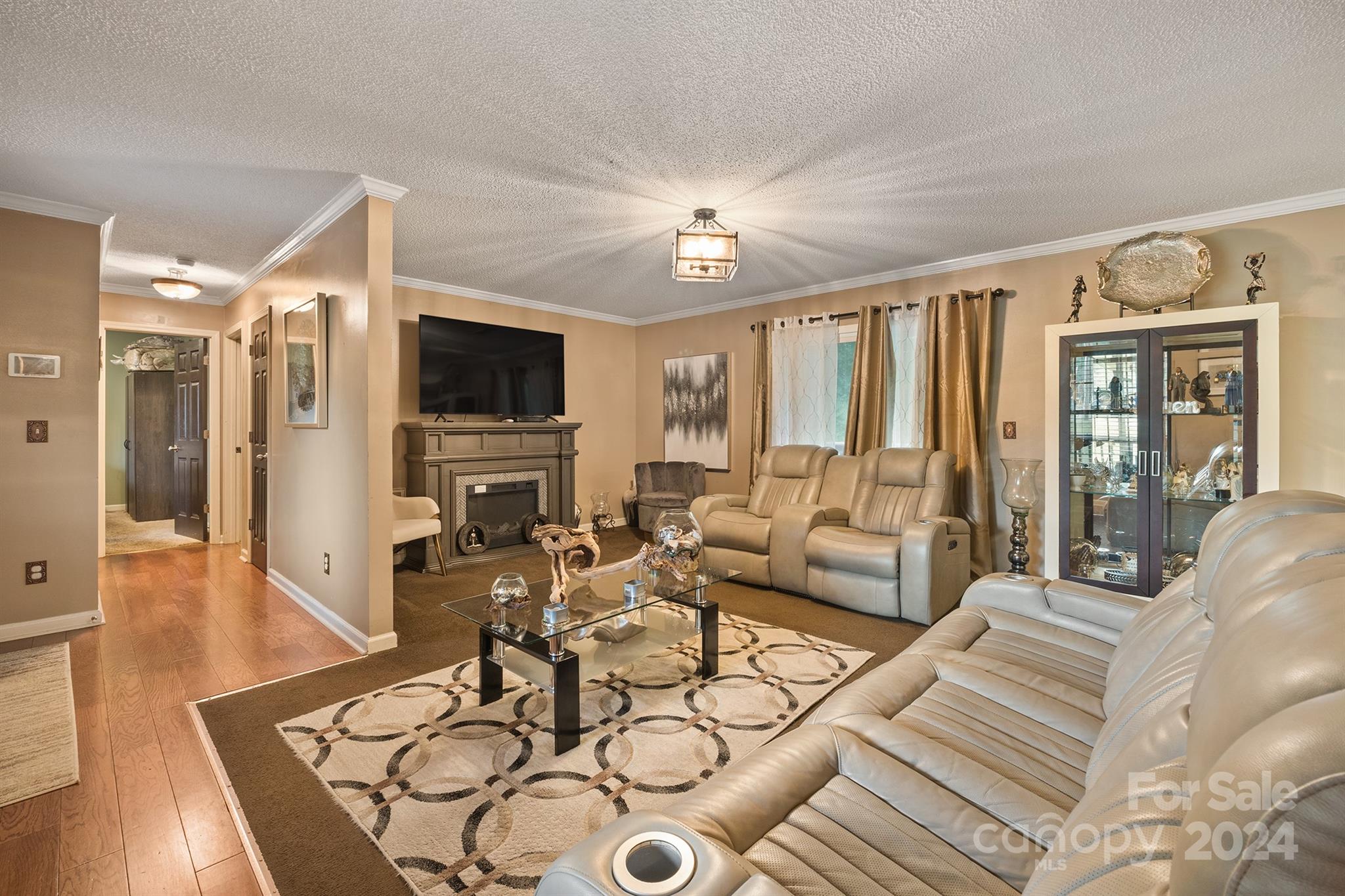 A stylish and spacious living room in a Charlotte, NC home for sale at 231 Nance Rd, boasting plush leather seating, a modern fireplace, wood flooring, and warm-toned walls with elegant décor and large windows...