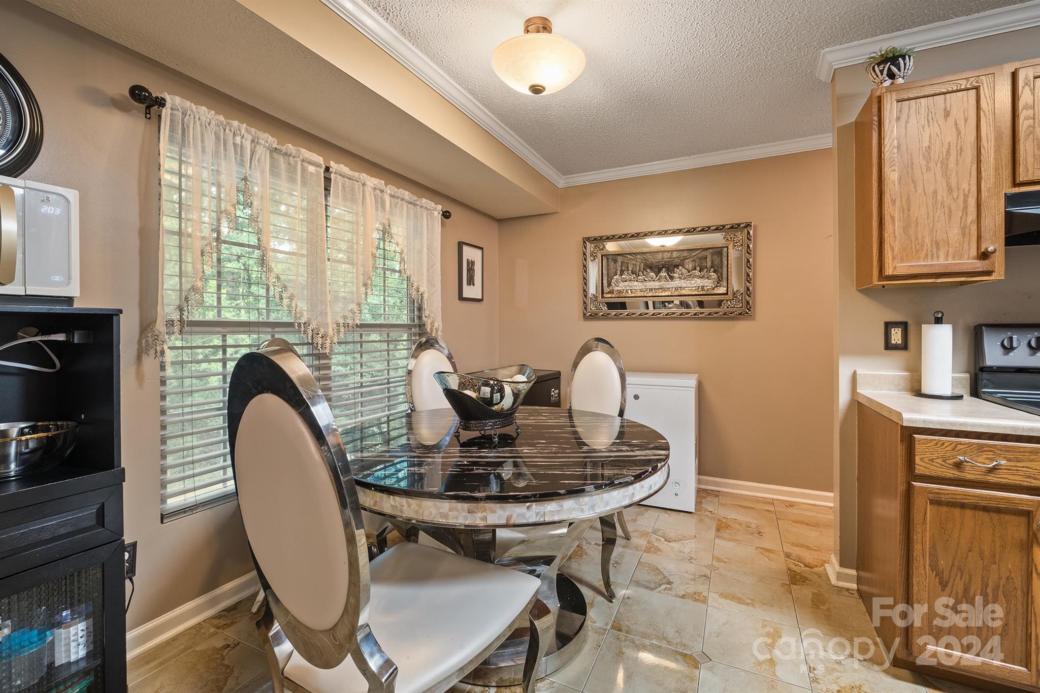 A warm and inviting dining area in a Charlotte, NC home for sale at 231 Nance Rd, featuring a round marble-top table, elegant high-back chairs, large windows with sheer curtains, and soft lighting creating a cozy ambiance...