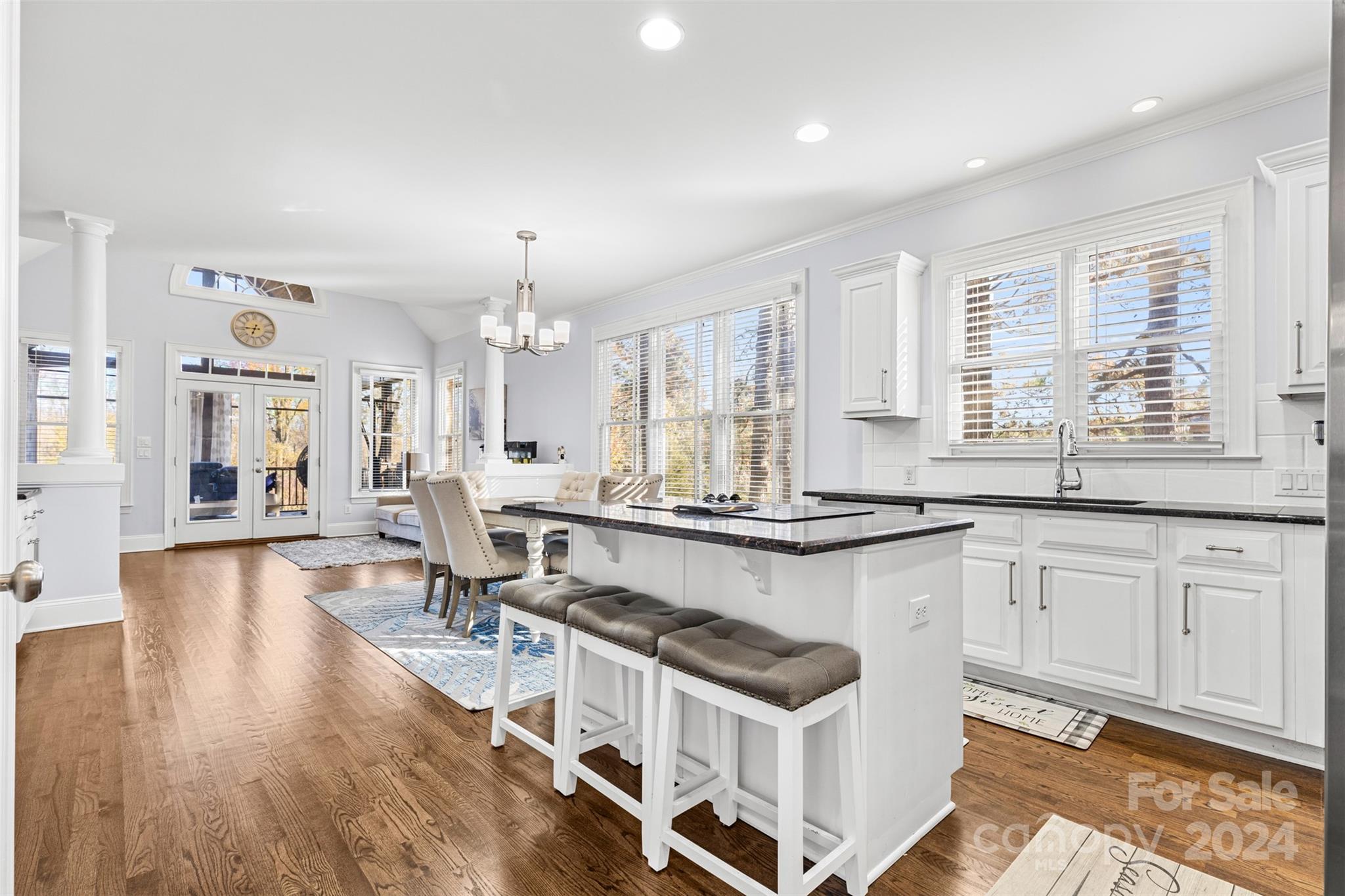 A stunning modern kitchen in a Huntersville, NC home for sale at 320 Three Greens Dr, showcasing white cabinetry, sleek granite countertops, a large island with bar seating, an open dining area, and floor-to-ceiling windows offering natural light...