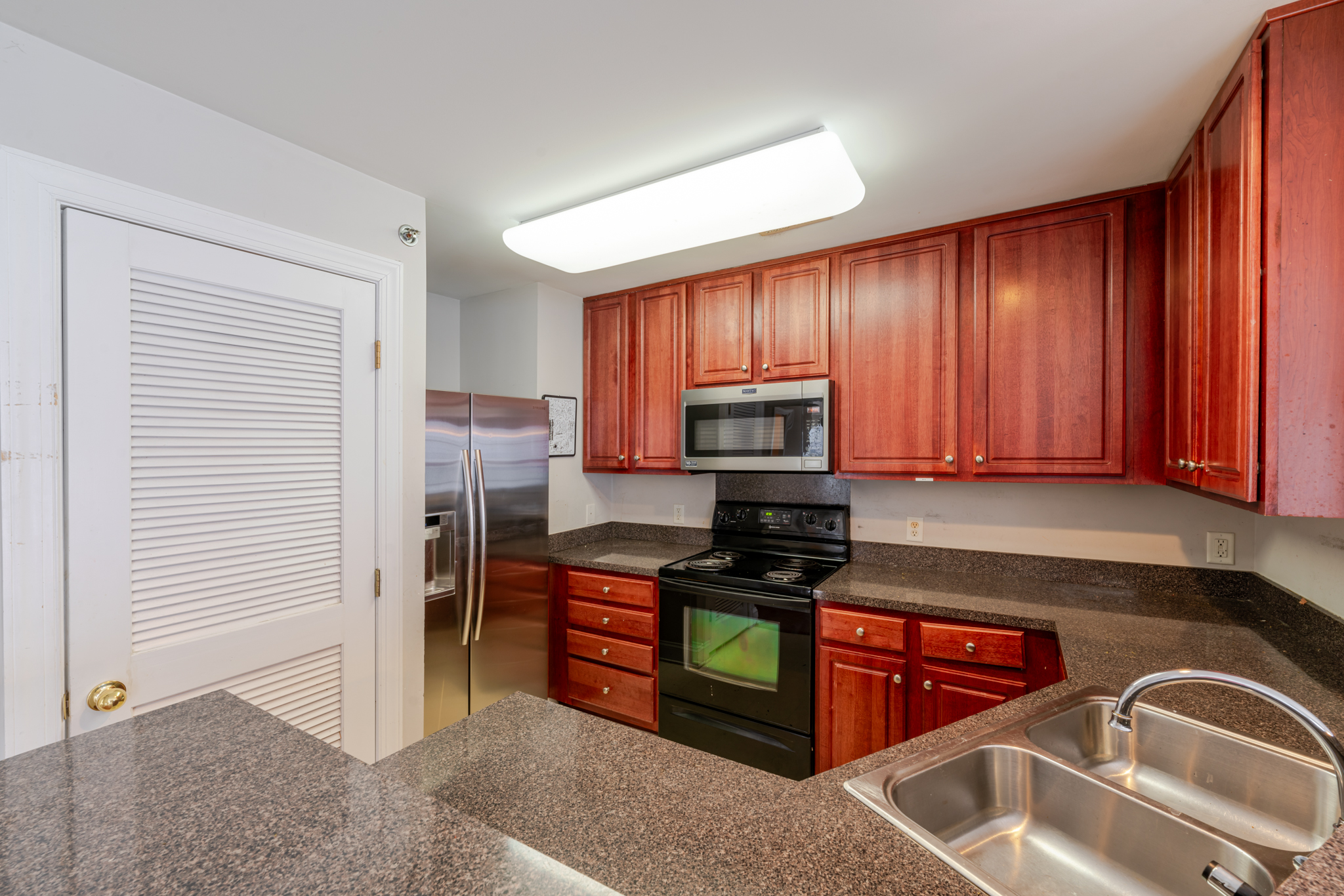 A modern kitchen in a Charlotte, NC townhome for sale at 6864 Park Place Dr, featuring cherry wood cabinetry, granite countertops, stainless steel appliances, a built-in microwave, and a sleek black electric range...