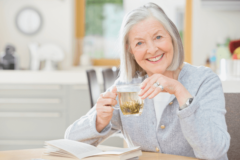 An older woman enjoying tea and reading a book in her bright, modern kitchen, symbolizing satisfaction and comfort in a Charlotte NC home. Highlighting Charlotte NC Homes for Sale and the expertise of Nancy Braun at Showcase Realty for top real estate services.
