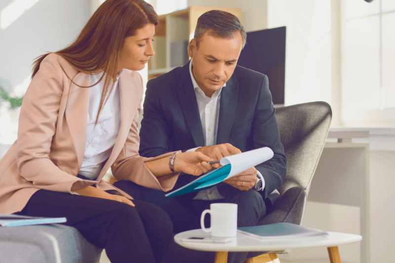 A professional real estate agent in a blush blazer sits with a serious-looking homebuyer in a modern, well-lit office. They carefully review property documents together, discussing important details about the Charlotte real estate market. Showcase Realty provides expert guidance, ensuring clients work with top Charlotte NC real estate agents to make informed home-buying decisions.
