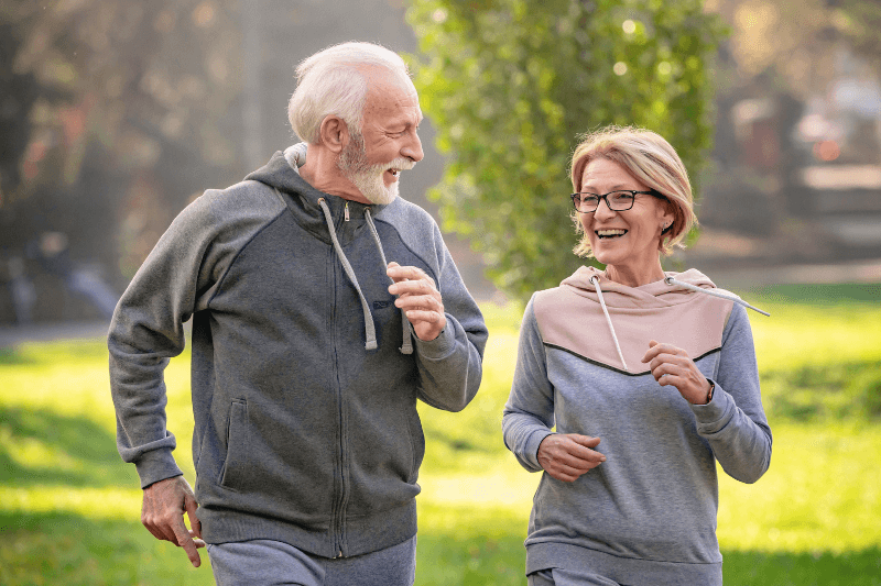 An active senior couple jogging together in a green park, representing the lifestyle benefits of living in a new construction home community in Charlotte, NC. This image highlights Charlotte NC Real Estate and the home buying opportunities available through Showcase Realty.
