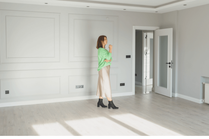 A woman in a stylish outfit standing in an empty modern home, thoughtfully considering the space. This image represents a prospective buyer exploring real estate options in the Charlotte housing market. The demand for homes in Charlotte, NC, continues to grow as buyers search for properties that match their needs in 2025.