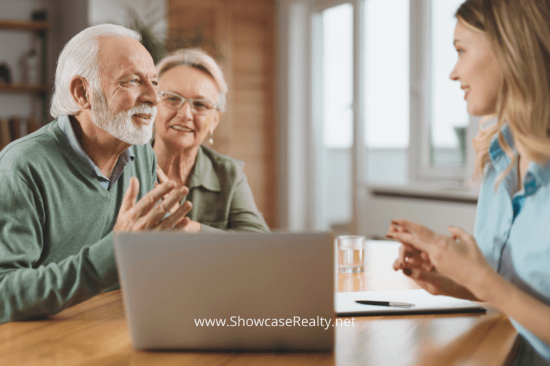 A smiling elderly couple sits at a table with a Charlotte NC real estate agent, engaged in a friendly conversation. The agent, dressed in a light blue shirt, is explaining details with a notepad and laptop in front of them. The couple looks attentive and pleased, reflecting a positive client-agent relationship. This image highlights the personalized service and client trust fostered by Charlotte NC real estate agents at Showcase Realty, representing the collaborative nature of the Charlotte real estate market.
