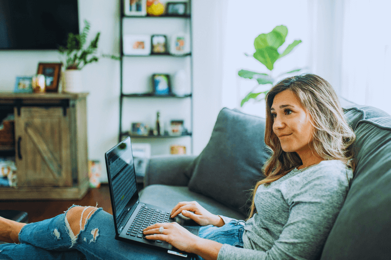 A woman sitting comfortably on a couch with her laptop, reflecting as she navigates the challenges of an empty nest. The image captures the personal journey many experience when considering Charlotte NC Home Buying and the changes that come with it, guided by Showcase Realty.
