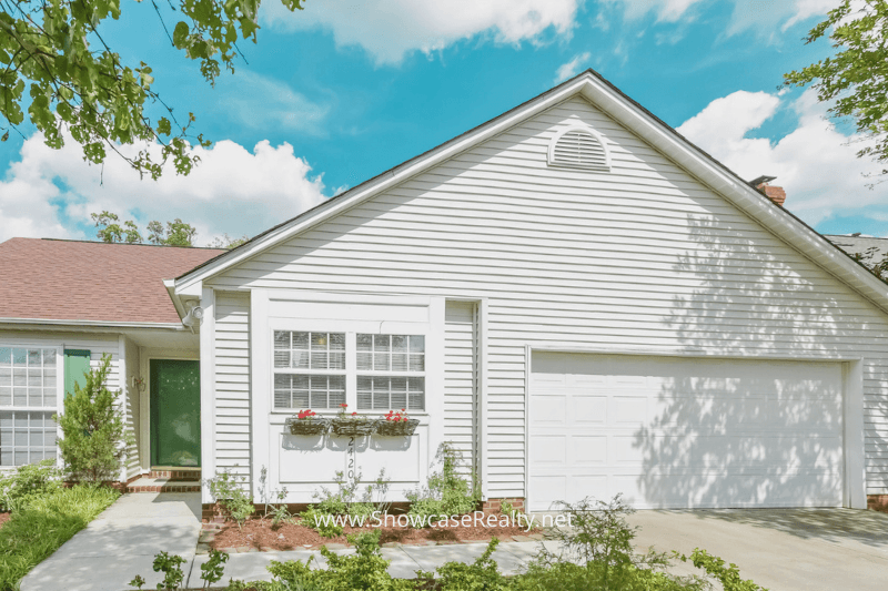 Front view of a charming white single-family home with a green door and two-car garage in a quiet Charlotte NC neighborhood, listed by Showcase Realty and ideal for first-time Charlotte NC home buying.
