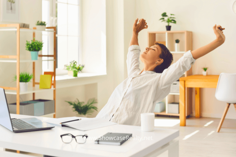 Relaxed woman stretching at her desk in a bright home office, symbolizing the relief and satisfaction after successfully navigating Charlotte NC home buying with help from Showcase Realty in the Charlotte NC real estate market.
