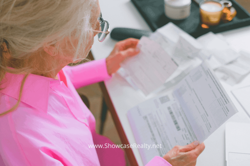 An older woman in a bright pink shirt reviews bills or HOA documents at a table, representing the financial considerations of Charlotte NC home buying. This moment highlights how Showcase Realty helps clients understand the true value of HOA fees in the Charlotte NC real estate market.