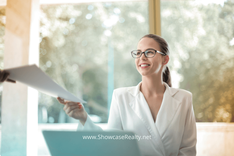 Smiling real estate agent in a bright office handing documents to a client — representing Showcase Realty’s commitment to professional Charlotte NC home selling services.
